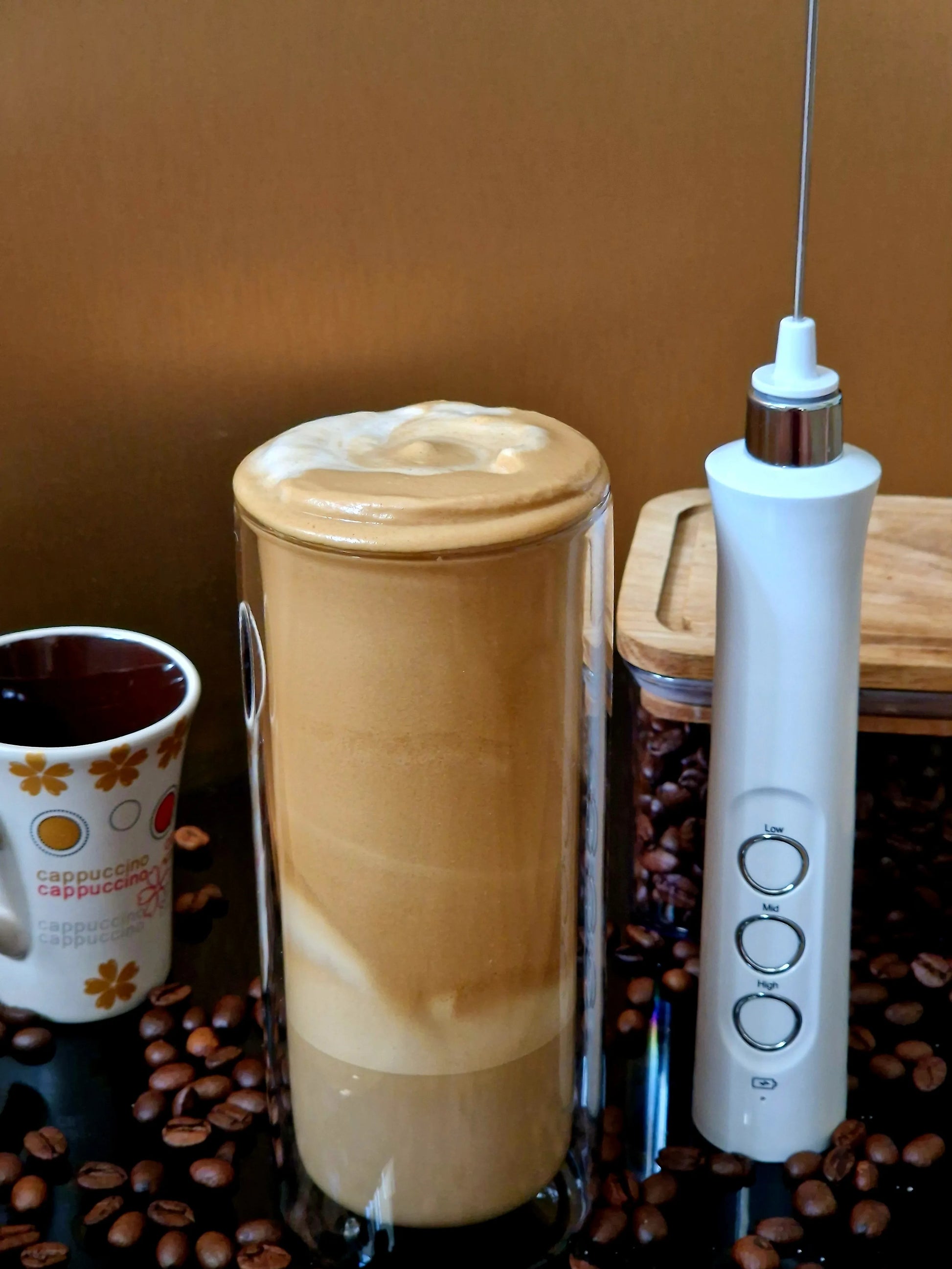 Mousseur à lait à côté d'un bocal de grains de café et d'une tasse de cappuccino