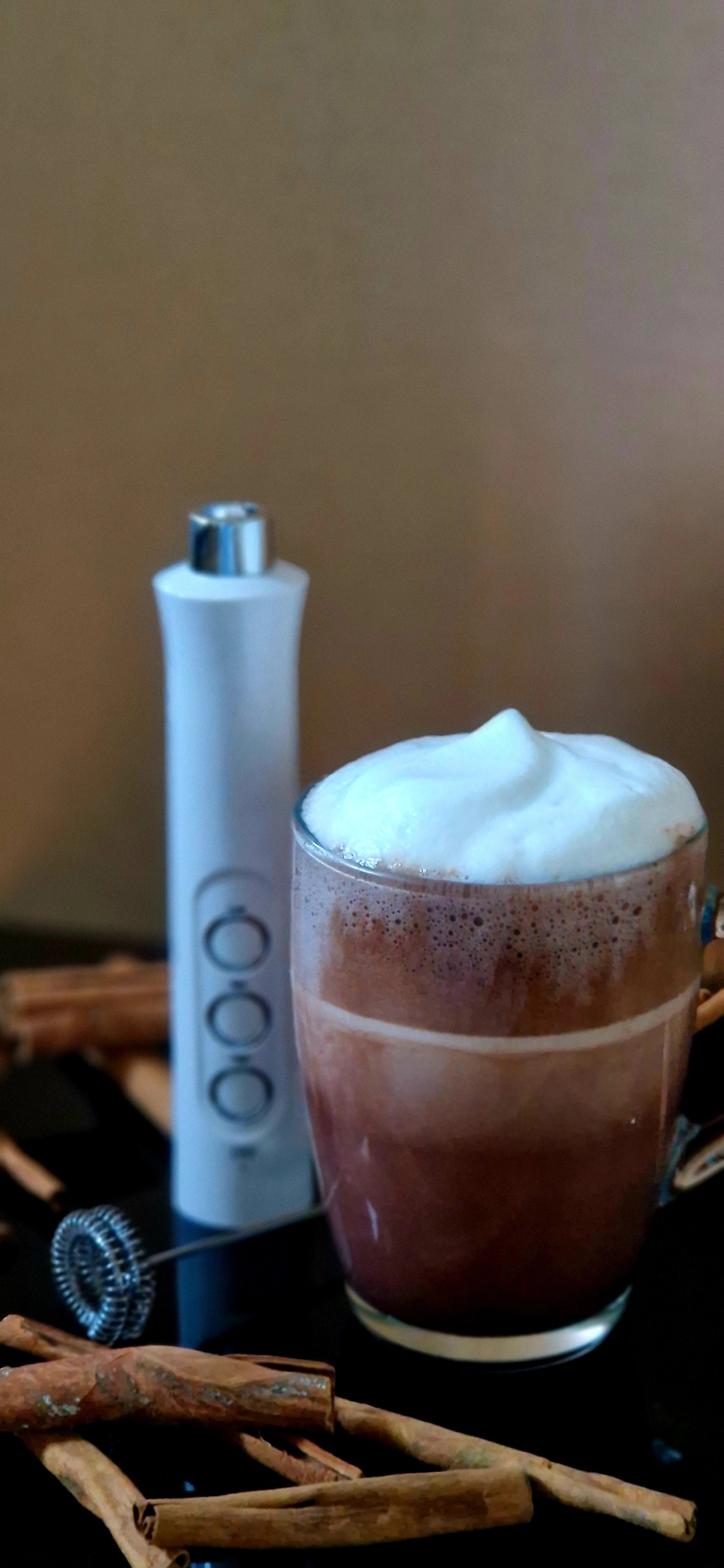 Tasse de café mousseux avec le mousseur à lait Mousseur Magique suspendu par son cordon, grains de café en arrière-plan